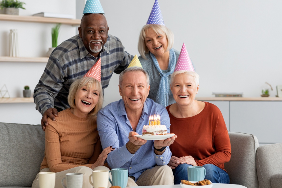 dos hombres y tres mujeres de mediana edad con pastel y gorros de cumpleaños