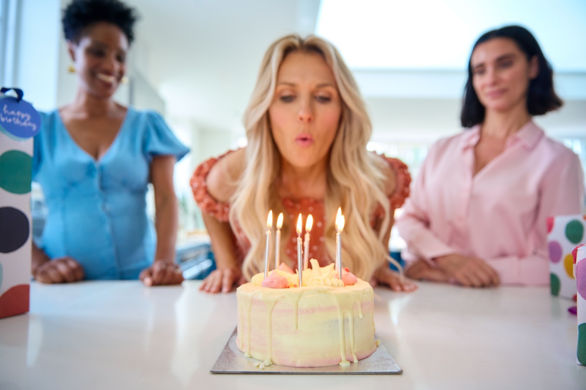 mujer soplando velas de cumpleaños y otras dos mujeres atrás