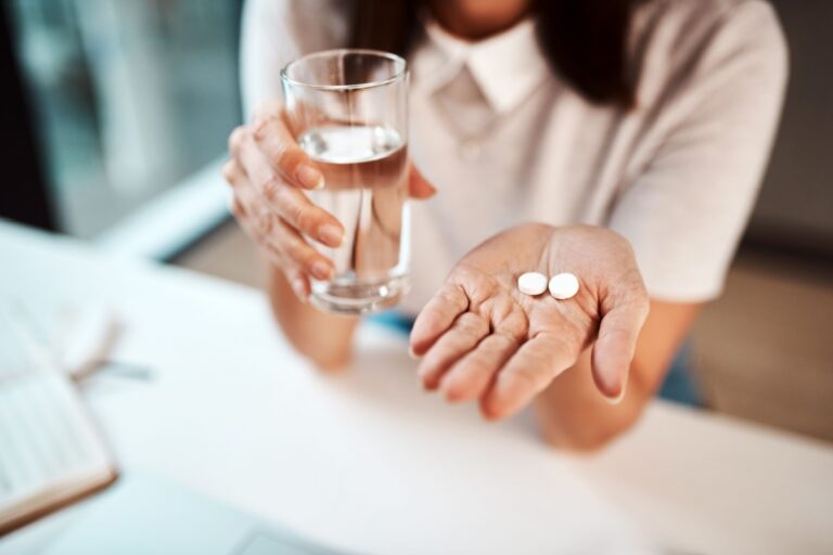 woman holding a glass of water and two pills