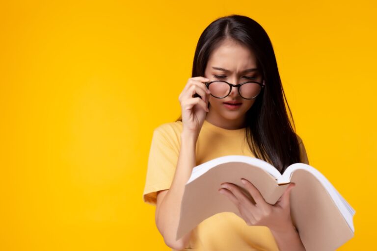 young woman with glasses making an effort to read a book