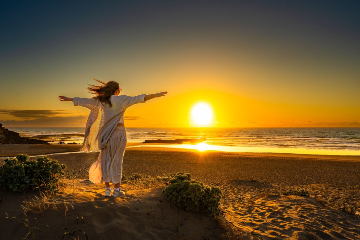 woman with the arms open at the beach during the sunset