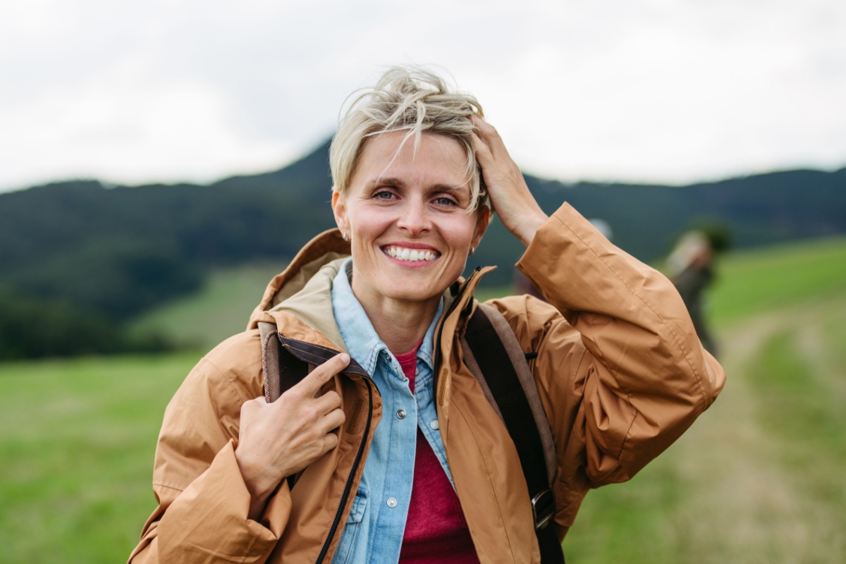 mujer de mediana edad en la naturaleza, sonriendo y tocándose la cabeza