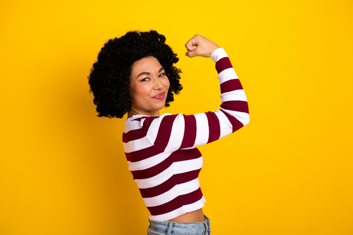 mujer con el brazo en alto en señal de fuerza, sobre fondo amarillo