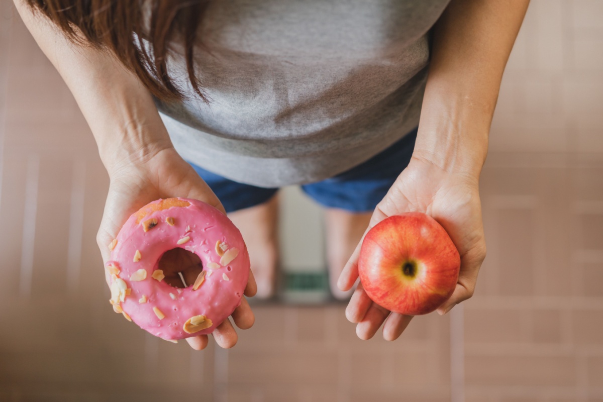 woman with an apple in one hand, and a donut in th other