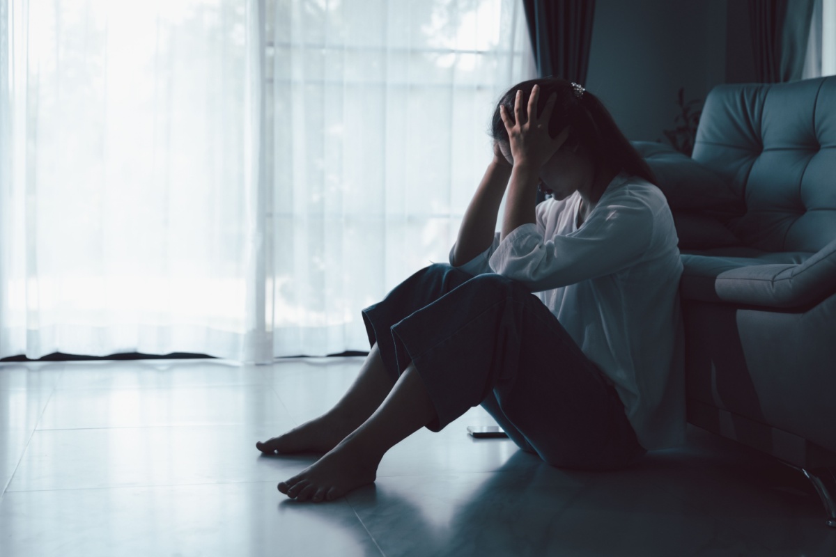 mujer sentada en el piso en la oscuridad tomándose la cabeza