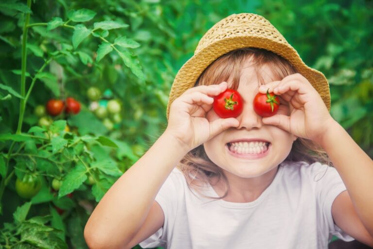 little girl holding cherry tomatoes in her eyes