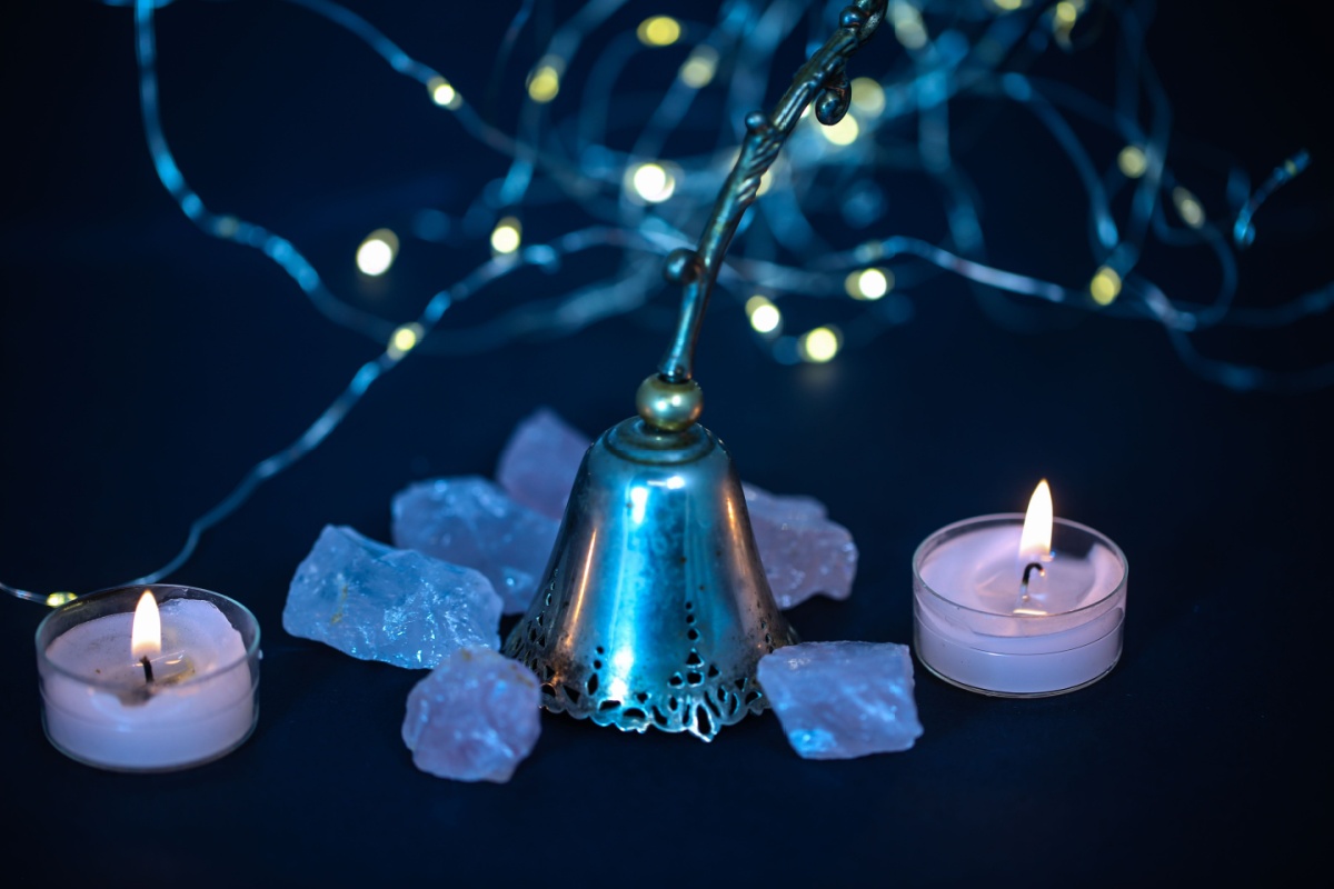 dos velas encendidas, una campana y varias piedras en fondo azul