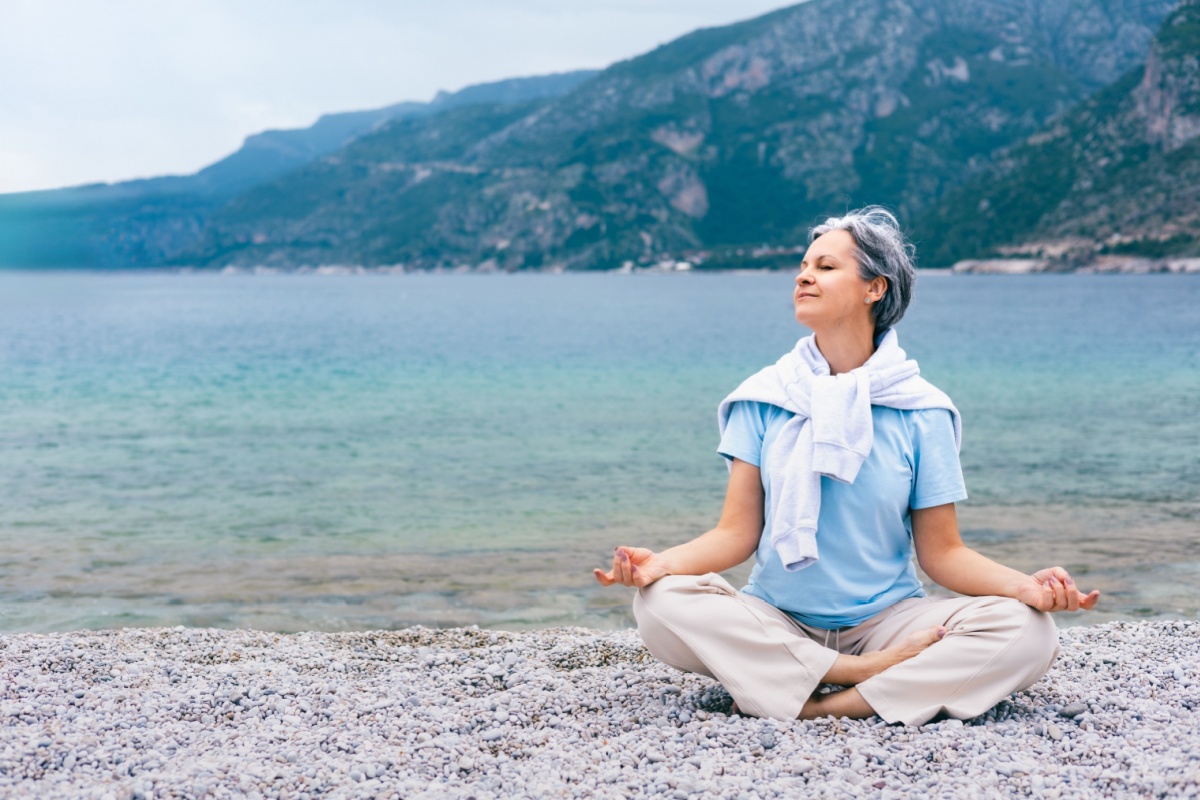mujer de mediana edad meditando a orillas de un lago