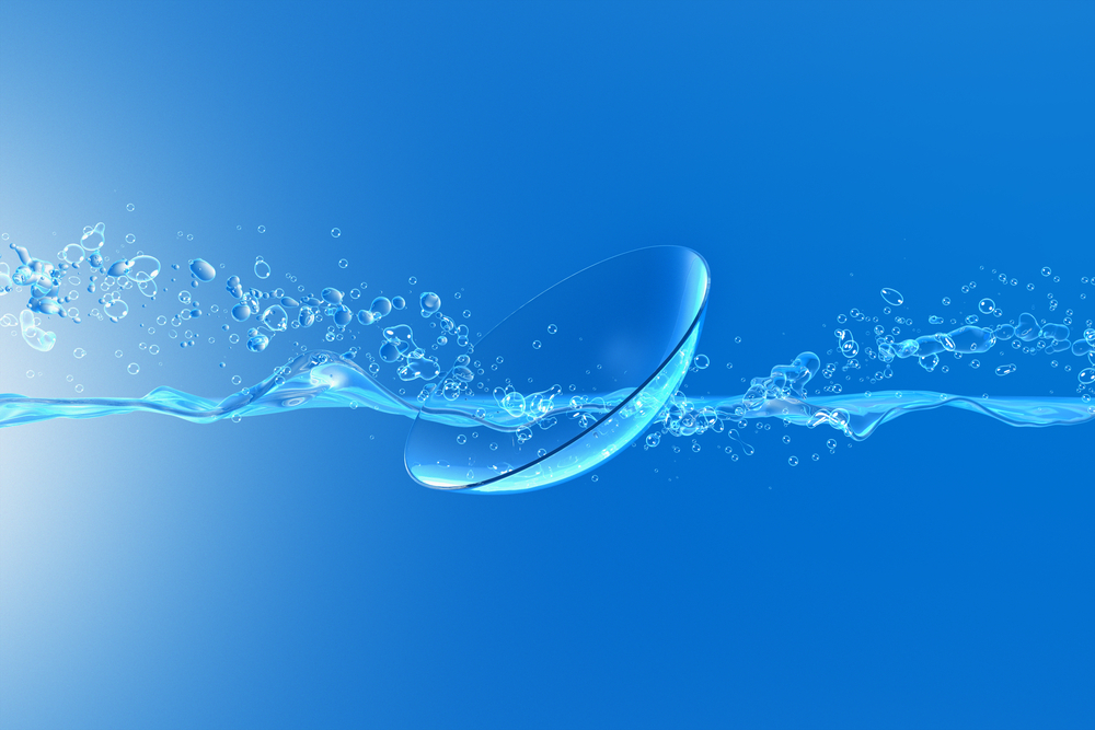 A photo-illustration of a contact lens and bubbles of transparent liquid across a blue background.