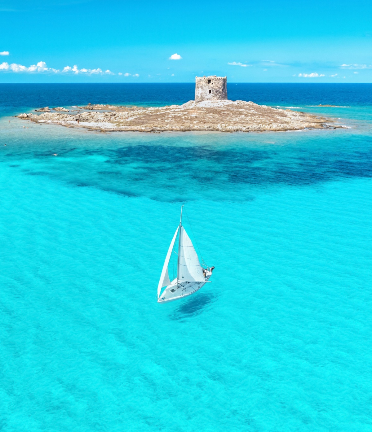 A sailboat sailing in beautiful blue water with a small desert island and a ruin in the background